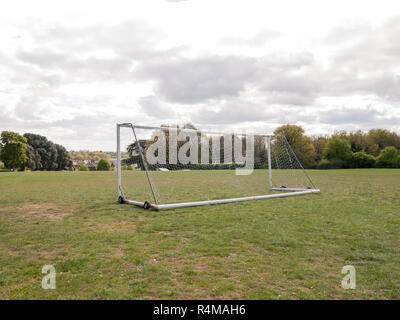 Une case vide et inutilisé poteau de but avec un filet blanc au milieu d'un parc d'herbe et de sol sur le terrain, les roues sur le châssis pour aider à déplacer et maisons et arbres en arrière-plan, utilisé pour le football et pour un gardien de but aucune personne vu de derrière Banque D'Images