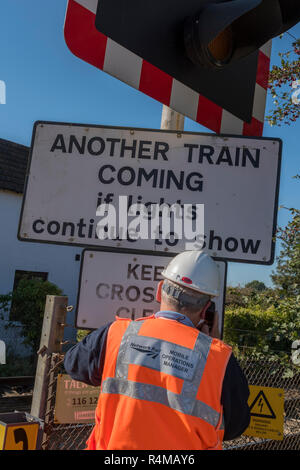 Network Rail worker wearing Vêtements haute visibilité un passage à niveau d'exploitation du téléphone. Un autre train venant d'avertissement et de signalisation. Banque D'Images