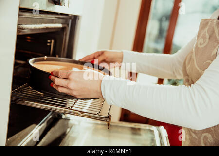 Femme met le gâteau fait maison dans le four Banque D'Images