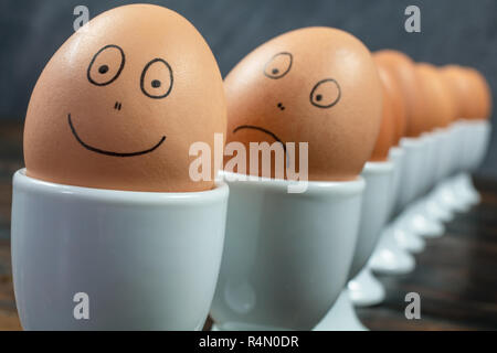 Concept d'attente ou s'aligner de dix œufs durs dans white egg cups avec appelée heureux et triste visages sur une table en bois Banque D'Images