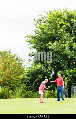 Senior woman and man playing golf putting on green Banque D'Images