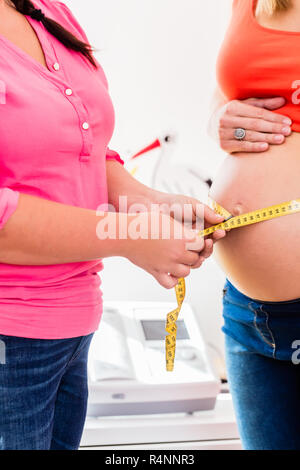 Les femmes enceintes et permanent de mesure de la circonférence de la sage-femme baby bump Banque D'Images