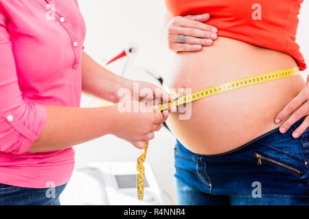 Les femmes enceintes et permanent de mesure de la circonférence de la sage-femme baby bump Banque D'Images