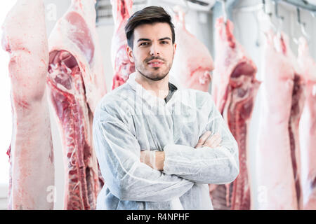 Travailleur dans une boucherie debout devant des carcasses Banque D'Images