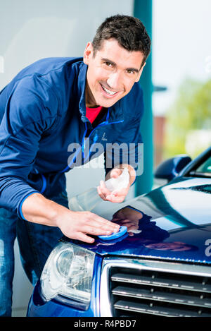 Happy man looking at camera while cirer une voiture bleue Banque D'Images