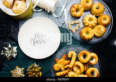 La plaque avec les salutations de Noël imprimé entouré de mini gâteau bundt et décoration sur une carte avec décoration de Noël, un paquet d'or et de ciseaux,t Banque D'Images