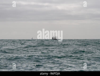 Bateau de pêche irlandais dans l'océan Atlantique au large des côtes de l'Irlande avec le phare du Fastnet à l'horizon. Banque D'Images