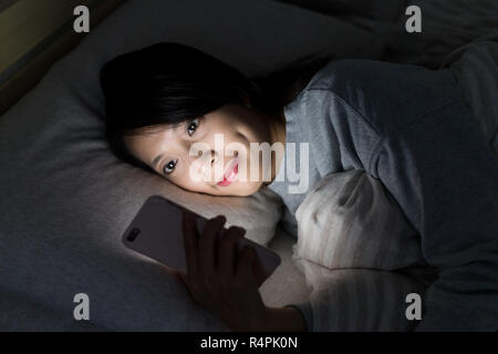 Woman using cellphone et couché sur le lit la nuit Banque D'Images