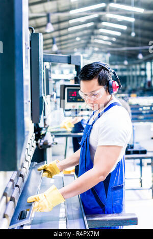 Deux des ouvriers de l'inspection de pièce à travailler debout sur le sol de l'usine avec cache-oreilles et des lunettes Banque D'Images