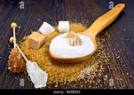 Brun et Blanc Sucre en cubes, granulé dans une cuillère et cristal sur un bâton dans le contexte d'une planche en bois Banque D'Images