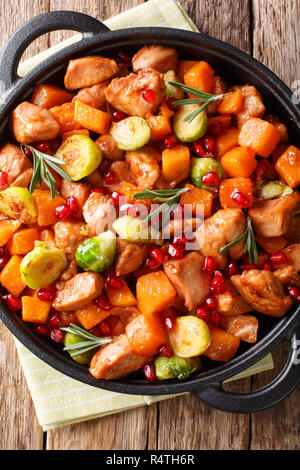 Ragoût de poulet avec des patates douces, choux de Bruxelles à la sauce de grenade close-up dans une poêle sur la table. Haut Vertical Vue de dessus Banque D'Images