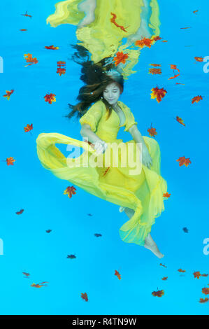Young woman in yellow dress posing sous l'eau, feuilles d'automne Banque D'Images