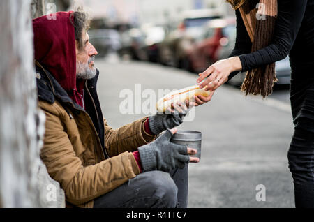 Femme méconnaissable en donnant de la nourriture aux sans-abri mendiant homme assis à l'extérieur dans la ville. Banque D'Images