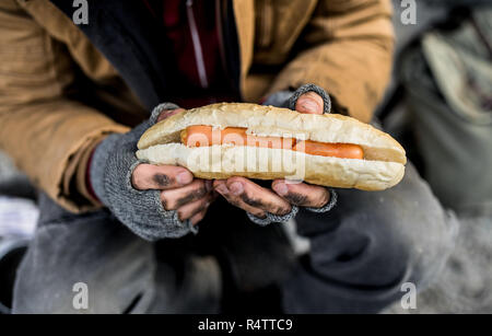 Portrait d'un homme sans-abri de mendiant à l'extérieur en ville, holding hot-dog. Un gros plan. Banque D'Images