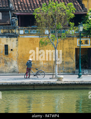 Hoi An une dame vietnamienne traditionnelle de rouler à vélo dans la vieille ville UNESCO de Hoi An au Vietnam. Banque D'Images