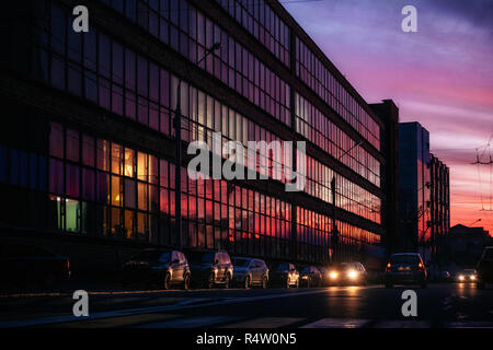 Bâtiment en verre avec ville en soirée et vibrant violet, orange et rouge Ciel de coucher du soleil à elle et les voitures dans la rue, Minsk, Biélorussie Banque D'Images