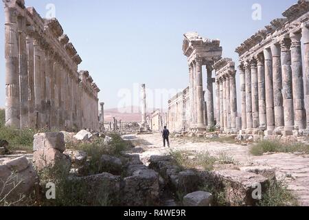 Paysage panoramique de la ruines antiques de la ville d'Apamée, Syrie, juin 1994. Un homme marche seul à travers la grande colonnade Cardo Maximus vers une colonne votive au milieu de l'avenue. () Banque D'Images