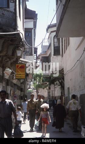 Scène d'une ruelle bordée de balcon bondé à Damas, en Syrie, en juin 1994. Au centre de la trame est une jeune fille l'équilibre entre un sac sur sa tête quand elle marche dans la rue remplie de mystères. À gauche est un grand panneau film Kodak publicité en anglais et en arabe. () Banque D'Images