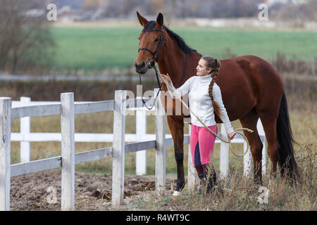 Jeune fille debout avec son bay horse près de paddock. Vie équestre contexte concept Banque D'Images