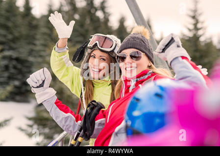 Belle jeune femme bénéficiant d'amis en vacances d'hiver. Ils la conduite sur la remontée mécanique et à la recherche à l'appareil photo avec sourire. Banque D'Images