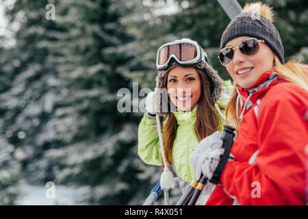 Belle jeune femme bénéficiant d'amis en vacances d'hiver. Ils la conduite sur la remontée mécanique et à la recherche à l'appareil photo avec sourire. Banque D'Images