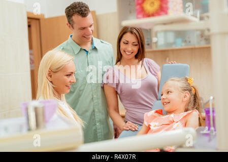 Famille heureuse à visiter dans le bureau de dentiste. Femme dentiste parlant avec petite fille, ses parents debout à côté d'elle. Banque D'Images