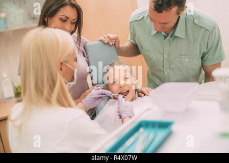 Famille heureuse à visiter dans le bureau de dentiste. Femme dentiste dents contrôle de la petite fille, ses parents debout à côté d'elle. Banque D'Images