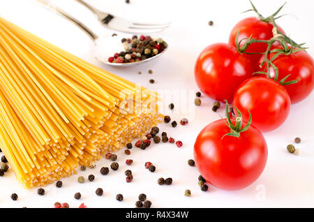 Ingrédients pour la cuisine italienne : Spaghetti se trouvent sur un fond blanc, ainsi que des tomates cerises, une cuillère dans laquelle se trouve le poivre et de la fourche Banque D'Images