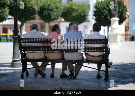 Quatre Espagnols assis, parlant, sur un banc dans un carré. Banque D'Images