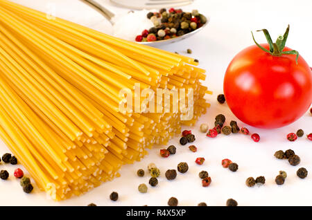 Ingrédients pour la cuisine italienne : Spaghetti se trouvent sur un fond blanc, ainsi que des tomates cerises, une cuillère dans laquelle se trouve le poivre et de la fourche Banque D'Images