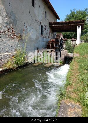 Un moulin à eau roue tourne en raison d'un petit ruisseau Cascade, au cours d'un été ensoleillé à Bellinzago, région du Piémont, Italie Banque D'Images