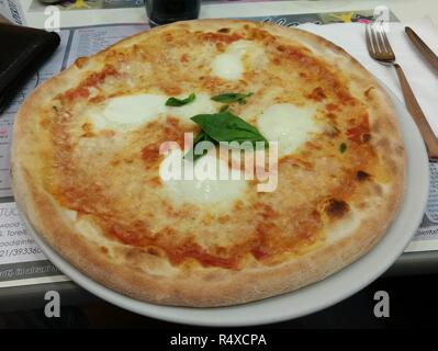 D'un original italien pizza Margherita sur un grand plat de céramique, avec un peu de basilic, à côté d'une fourchette sur une table Banque D'Images
