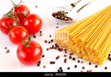 Ingrédients pour la cuisine italienne : Spaghetti se trouvent sur un fond blanc, ainsi que des tomates cerises, une cuillère dans laquelle se trouve le poivre et de la fourche Banque D'Images