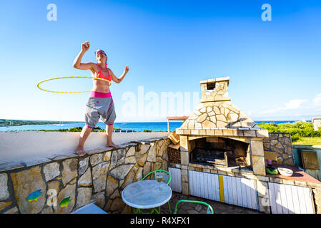 Jolie femme adulte joue avec cerceau dans la nature. Jeune, en bonne santé, active hipster femme est le hula hoop sur jardin méditerranéen avec vue sur Banque D'Images