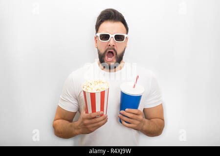 L'homme excité garde la bouche ouverte. Il est titulaire d'seau de popcorn et verre de cola en même temps. Guy porte des lunettes vidéo. Isolé sur fond blanc. Banque D'Images