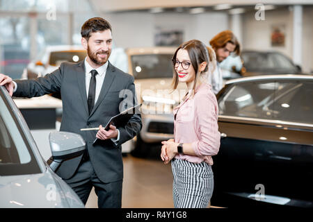 Vendeur de voiture pour aider une jeune femme client de prendre décision montrant une nouvelle voiture à l'exposition Banque D'Images