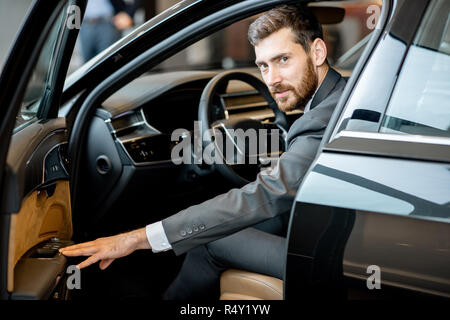Portrait of a handsome businessman assis sur le siège conducteur d'une voiture de luxe dans le showroom Banque D'Images