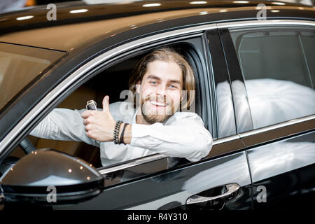 Portrait d'un heureux propriétaire assis sur un siège du pilote d'une nouvelle voiture de luxe à la salle d'exposition Banque D'Images