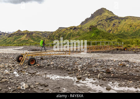 Le dirigeant d'une female hiker crossing un petit pont, portable, traversant une petite rivière sur le sentier Laugavegur en Islande. Banque D'Images