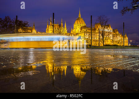 Budapest, Hongrie - Allumé Le Parlement de Hongrie à l'heure bleue avec réflexion et de tramway jaune traditionnelle en mouvement Banque D'Images