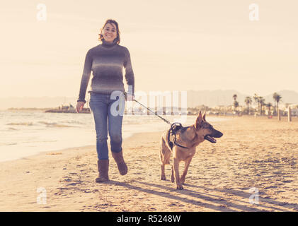 Belle femme adulte et pet German Shepard promenade de chiens le long de la côte de l'océan de la mer sur la plage au coucher du soleil de l'après-midi en compagnie d'animaux Prestations t Banque D'Images