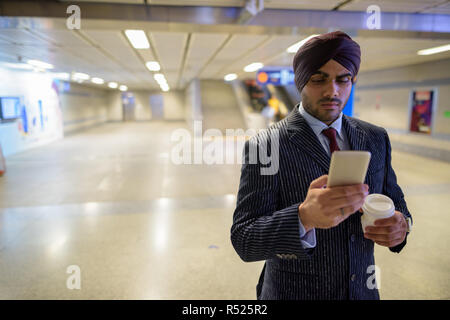 Homme d'affaires sikh indien au subway gare à l'aide de téléphone et holding coffee Banque D'Images