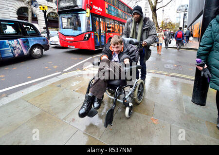 Homme handicapé dans un fauteuil roulant d'être poussé vers le bas le Strand, le centre de Londres, Angleterre, Royaume-Uni. Banque D'Images