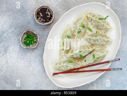 Korean quenelles avec la viande et les légumes sur une plaque blanche avec du sésame, de la sauce de soja et les oignons verts sur une surface de béton gris. La cuisine asiatique. Selectiv Banque D'Images