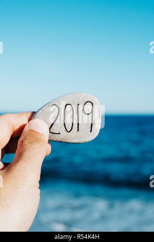 Libre d'un jeune homme avec une pierre dans sa main, avec le numéro 2019, comme la nouvelle année, écrits en C, sur la plage, avec l'océan dans le background Banque D'Images