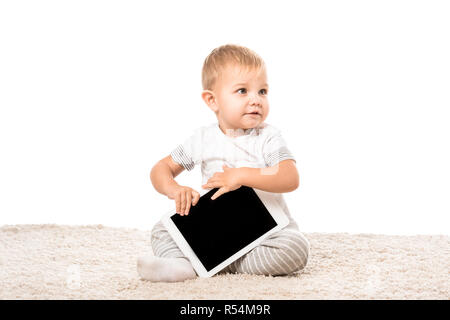 Beau Bébé garçon assis sur un tapis et holding digital tablet isolated on white Banque D'Images