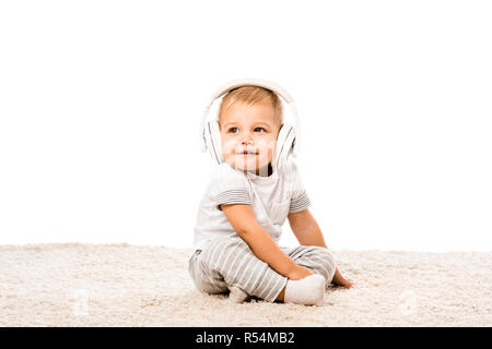 Tout-petit garçon assis sur un tapis avec headphones isolated on white Banque D'Images