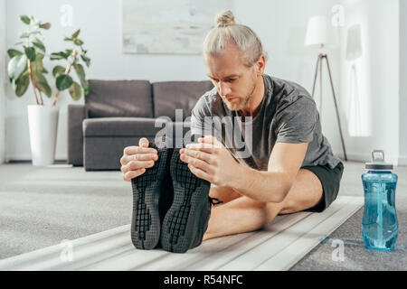 L'homme athlétique dans les vêtements de sport et l'exercice de stretching on yoga mat à la maison Banque D'Images