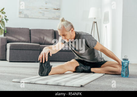 Athletic man in sportswear assis sur un tapis de yoga et stretching à la maison Banque D'Images