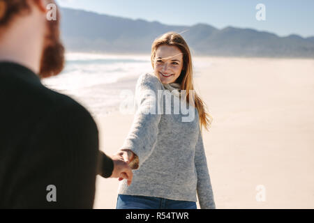Smiling woman holding la main de l'homme en marchant sur la plage. Happy young couple en train de marcher le long de la côte se. Banque D'Images